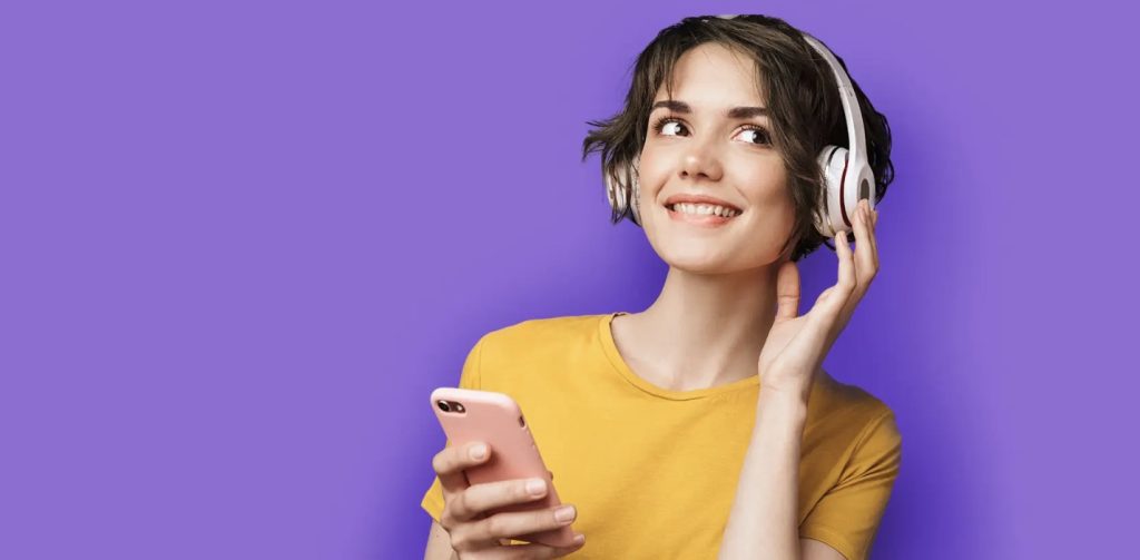 Frau im gelben T-Shirt mit einem Handy in der Hand und einem Kopfhörer auf den Ohren