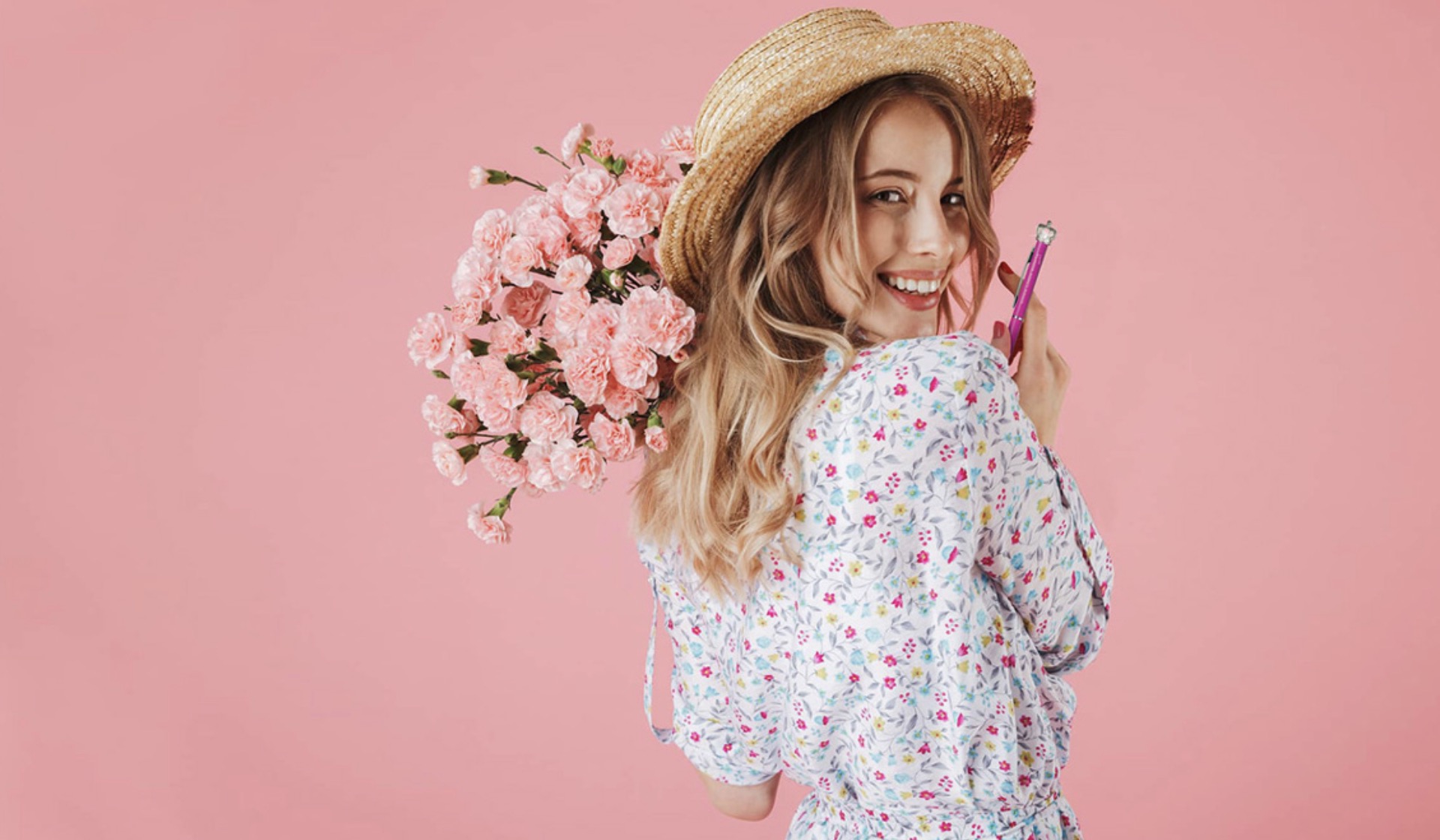 Eine Frau im Kleid die mit einem rosa Blumenstrauß über ihre Schulter guckt, grinst und einen Kugelschreiber in der Hand hält.